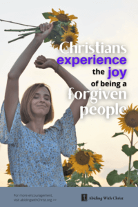 Link to Pinterest pin image of woman with eyes closed holding a handful of sunflowers over her head with text that reads "Christians experience the joy of being a forgiven people". 