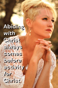 click link to Pinterest pin with image of woman outdoors leaning forward with hands clasped with text that reads "Abiding with Christ always comes before activity for Christ". 