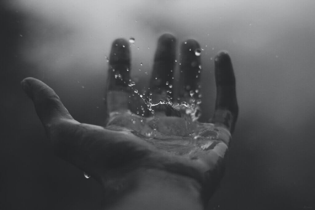 Black and white photo of hand catching a large raindrop, because we need to learn to be praising God in the storm.