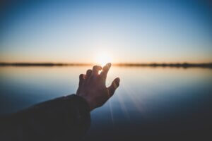 Hand reaching out to the sunrise; Jesus invites us to come and see.